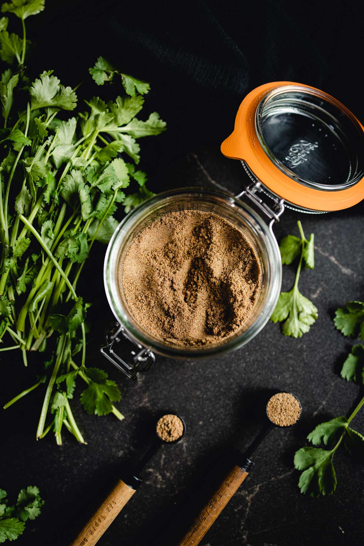 Coriander powder in a glass jar on a black table.