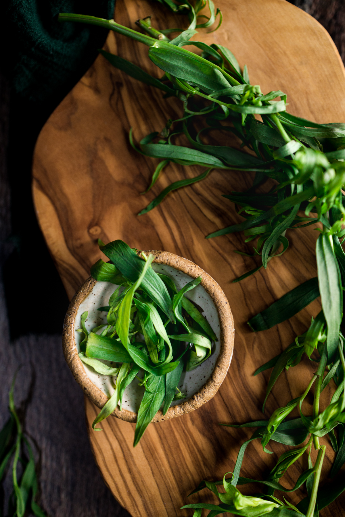 A bowl of tarragon greens on a wooden cutting board.