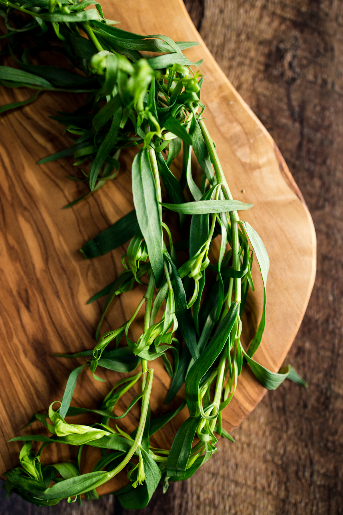 A bunch of green herbs on a wooden cutting board.