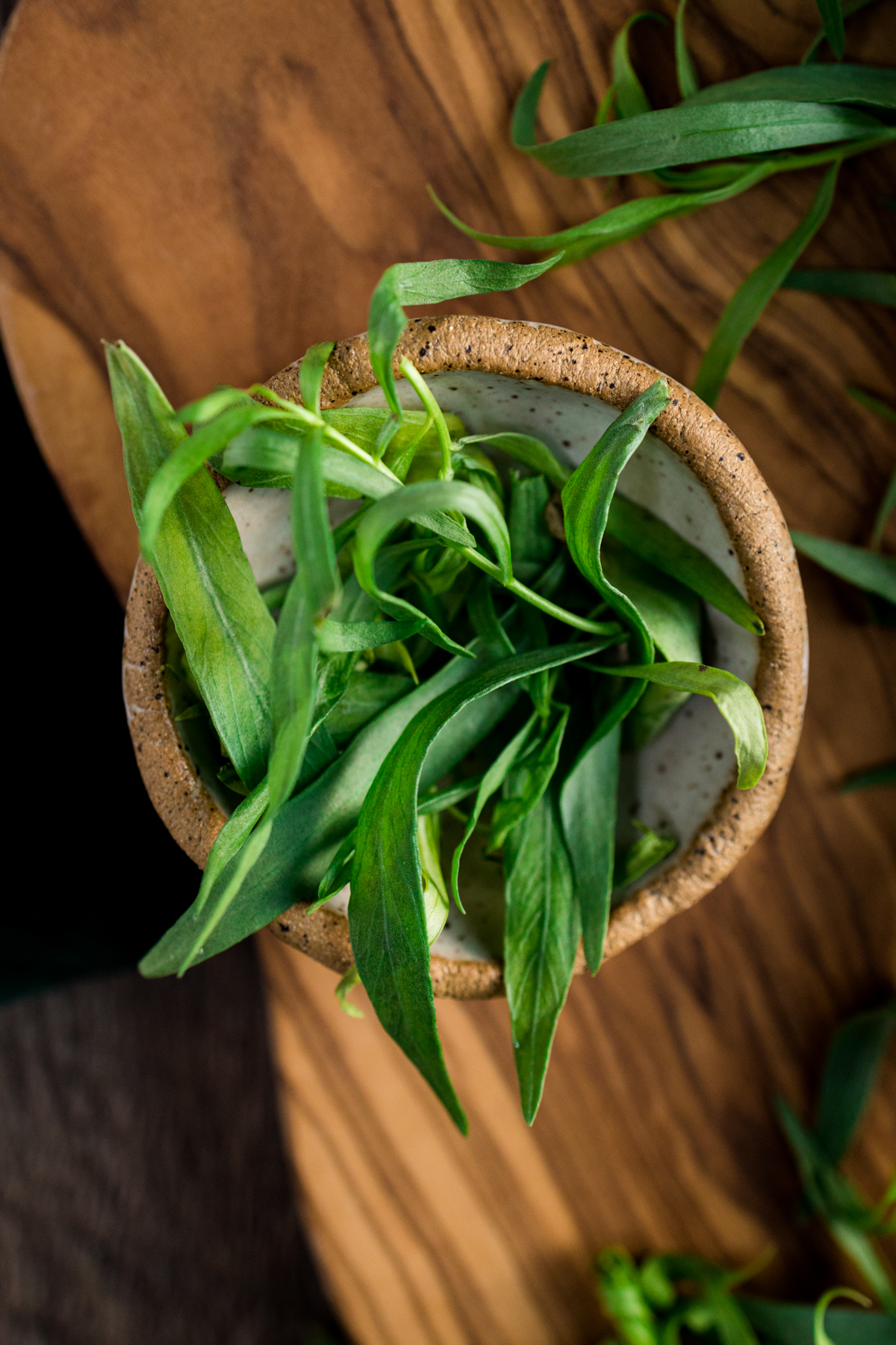 A bowl of tarragon leaves on a wooden table.
