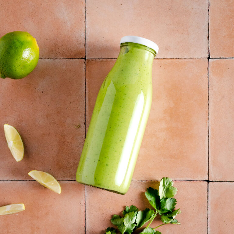 A bottle of green dressing with limes on a tiled table.