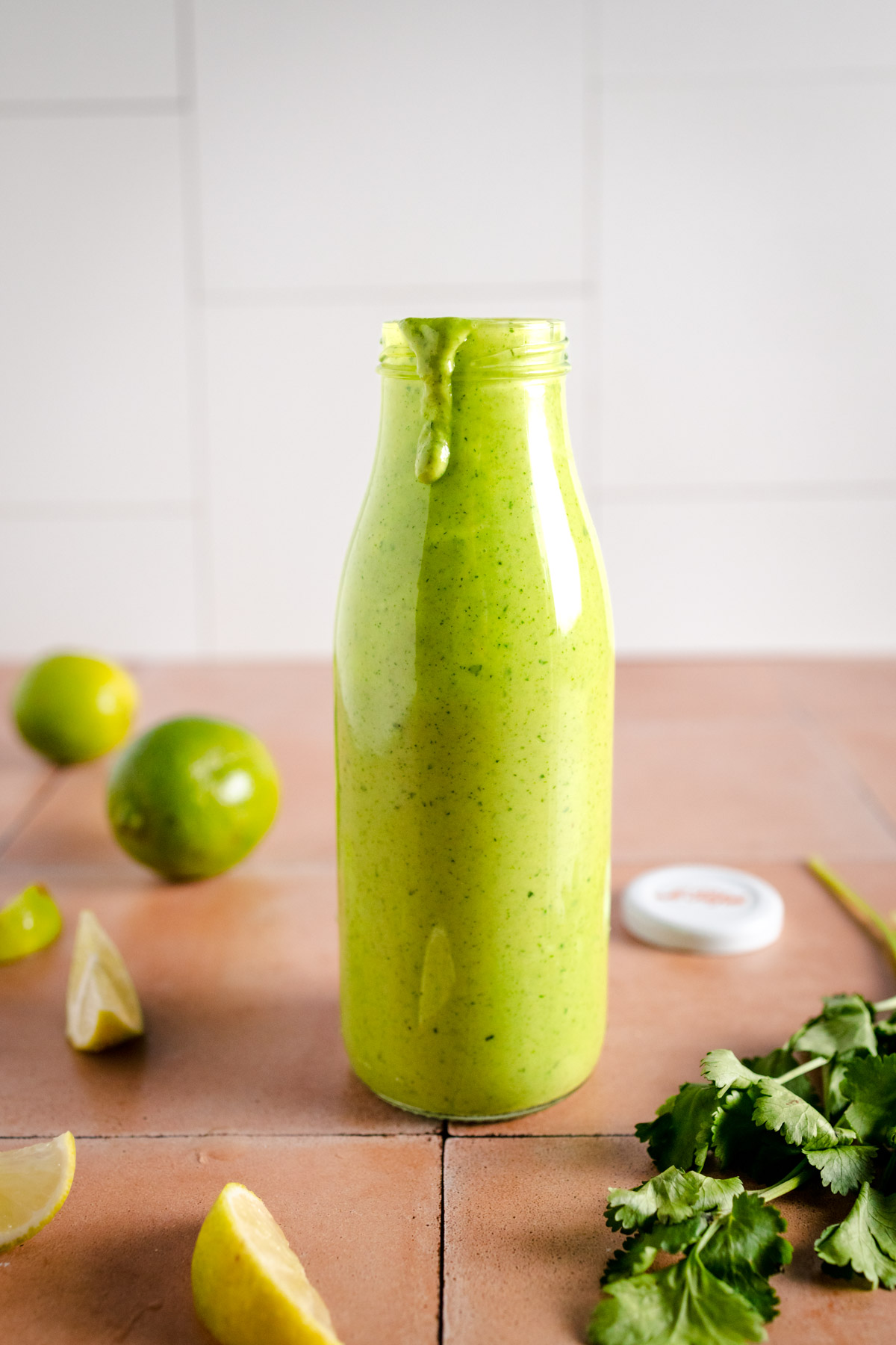 Cilantro lime dressing in a Le Parfait bottle with fresh lime and cilantro surrounding it.