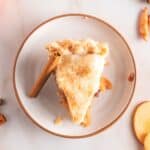 A slice of apple pie with a flaky crust sits on a white plate.