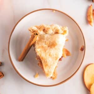 A slice of apple pie with a flaky crust sits on a white plate.