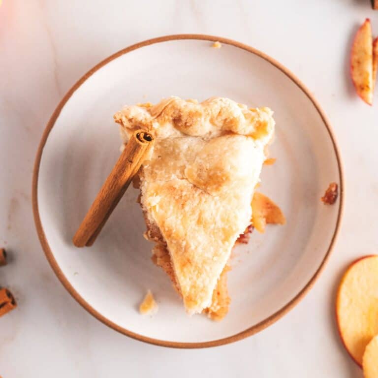 A slice of apple pie with a flaky crust sits on a white plate.