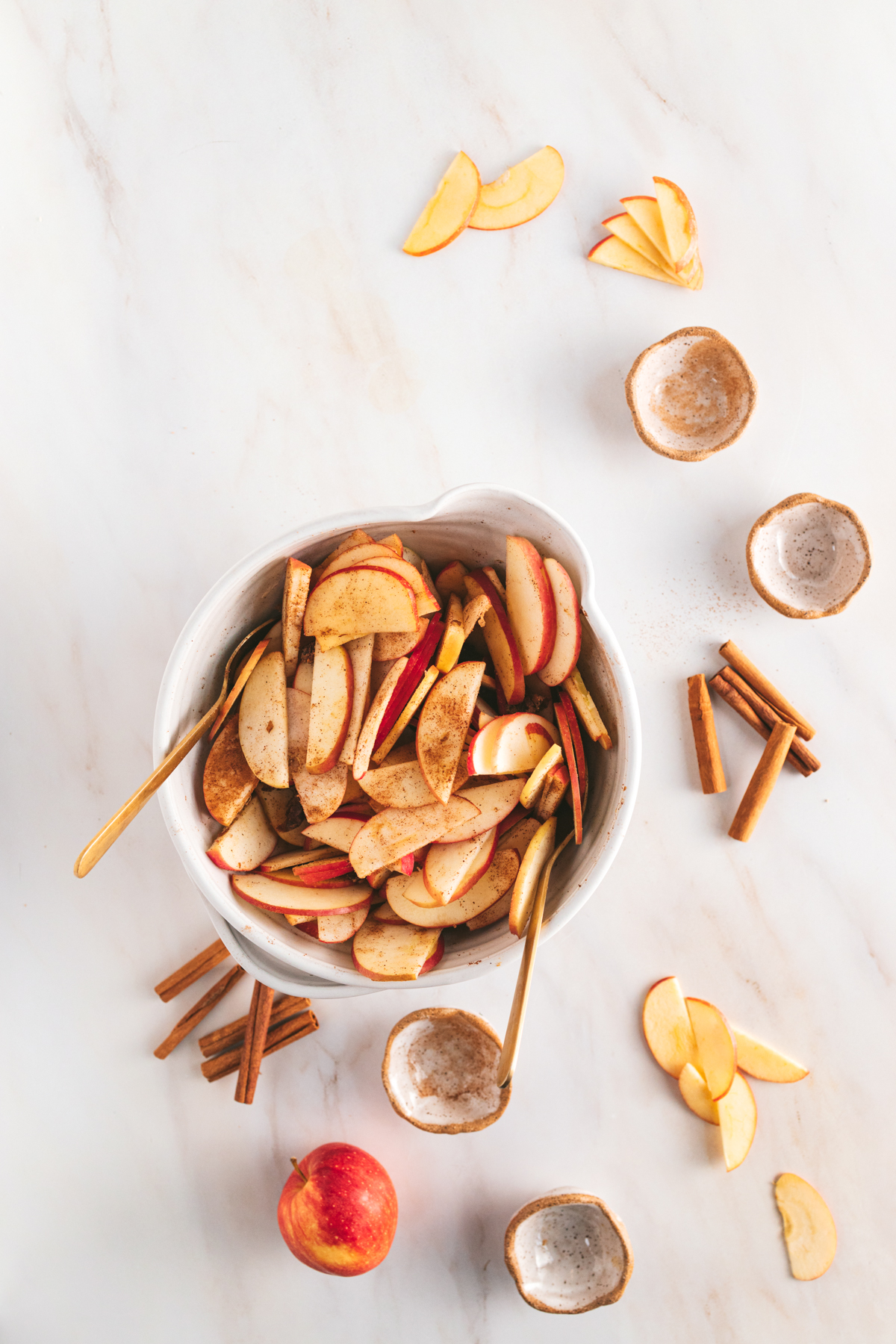 Apple slices in a bowl with cinnamon sticks.