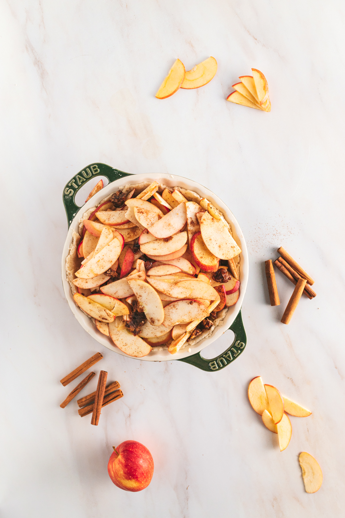 Apple pie in a dish with cinnamon sticks and apples.