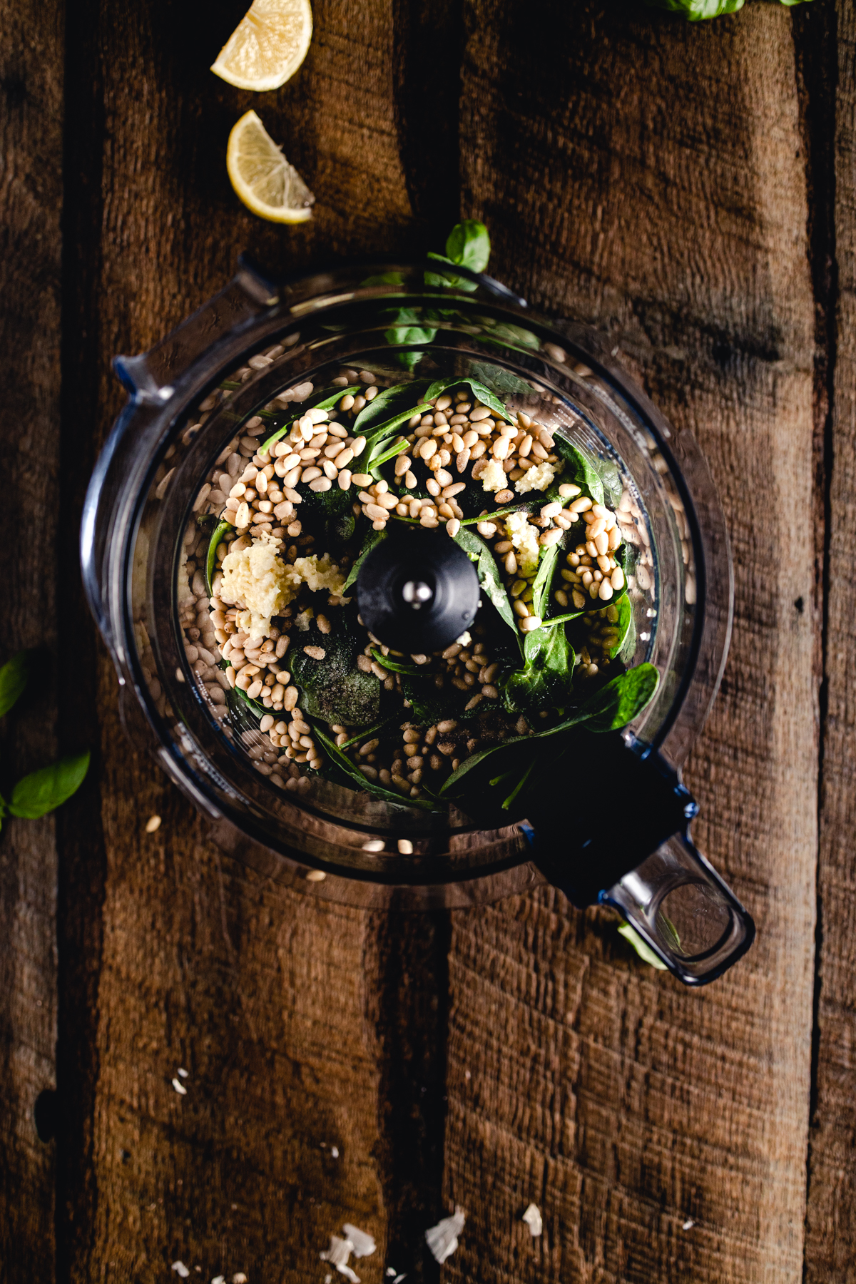 A blender filled with herbs and nuts on a wooden table.