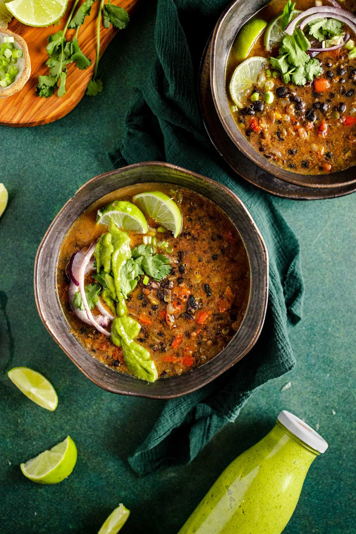 Two bowls of black bean soup on a green background.