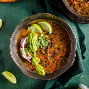 One bowl of black bean soup on a green table.