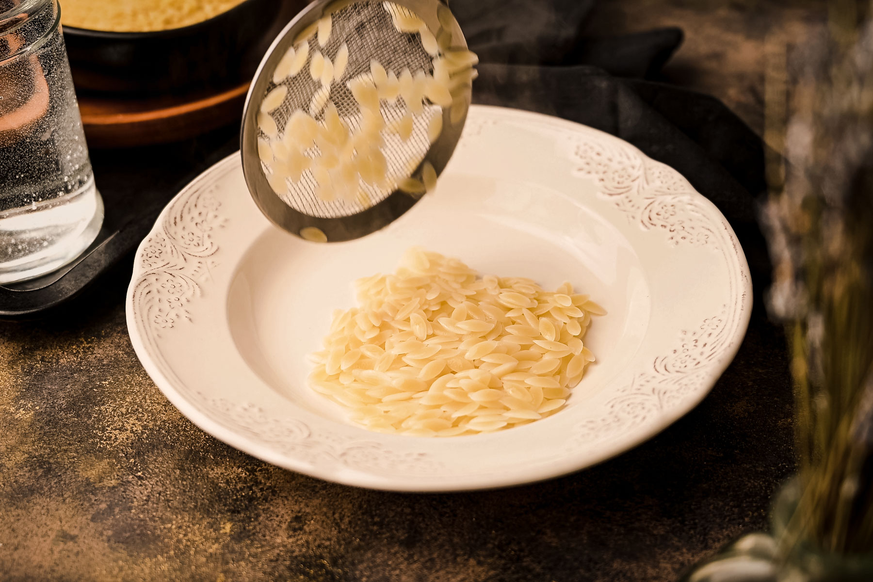 Orzo in a white bowl next to a glass of water.