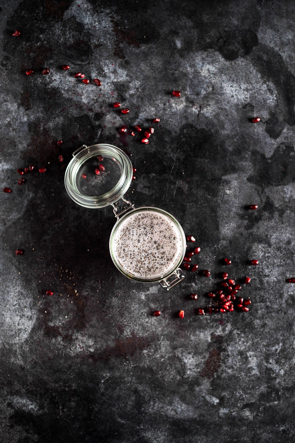 Pomegranate seeds in a glass container on a dark background.