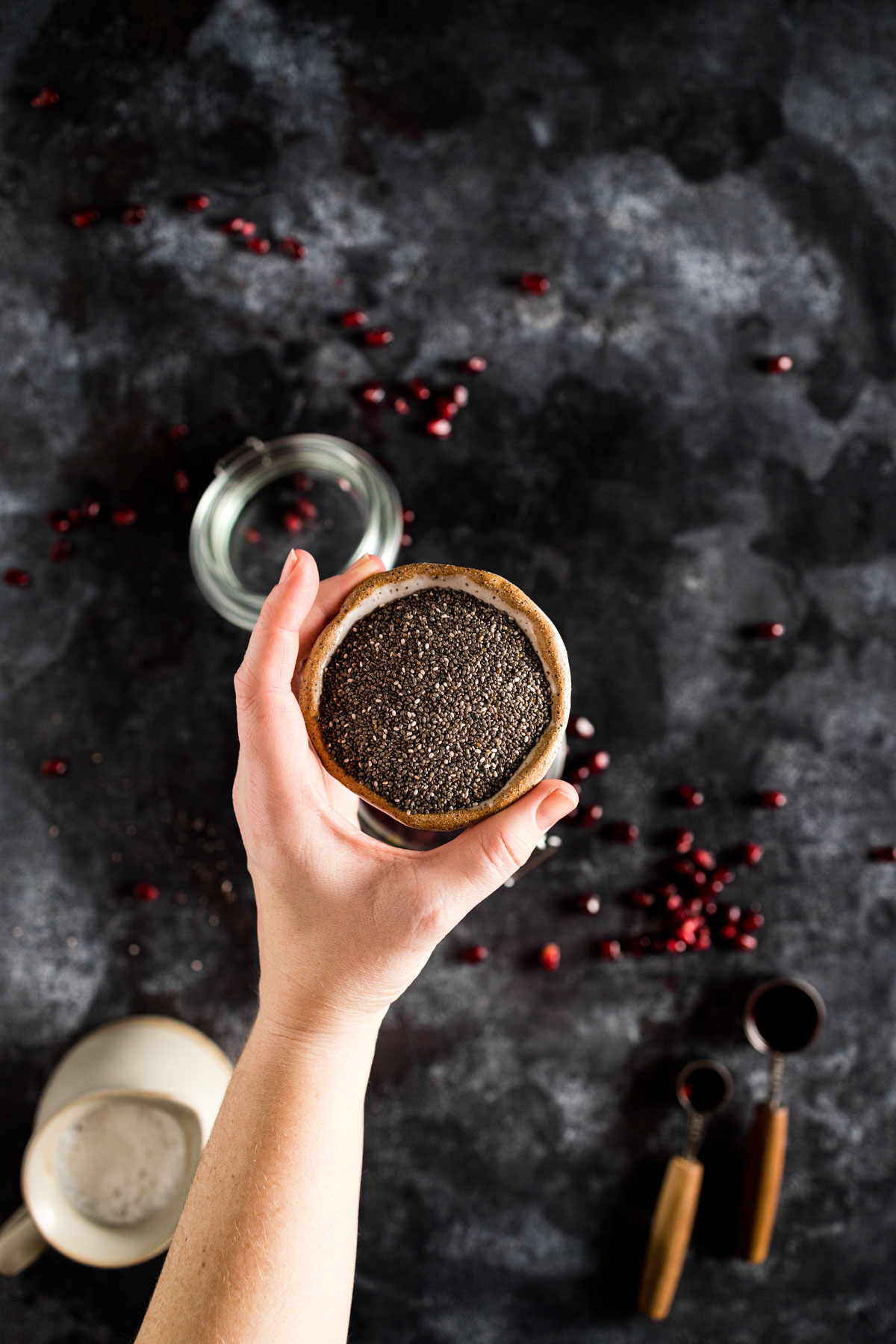 A hand holding a cup of chia seeds on a dark background.