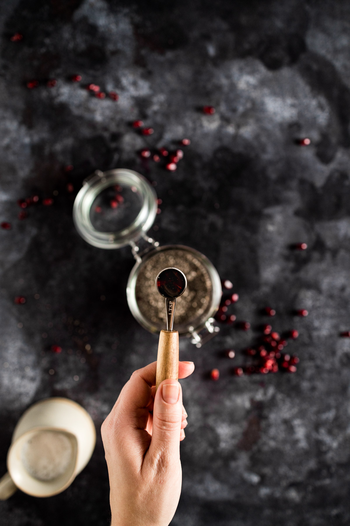 A hand is holding a spoon with cranberries in it.