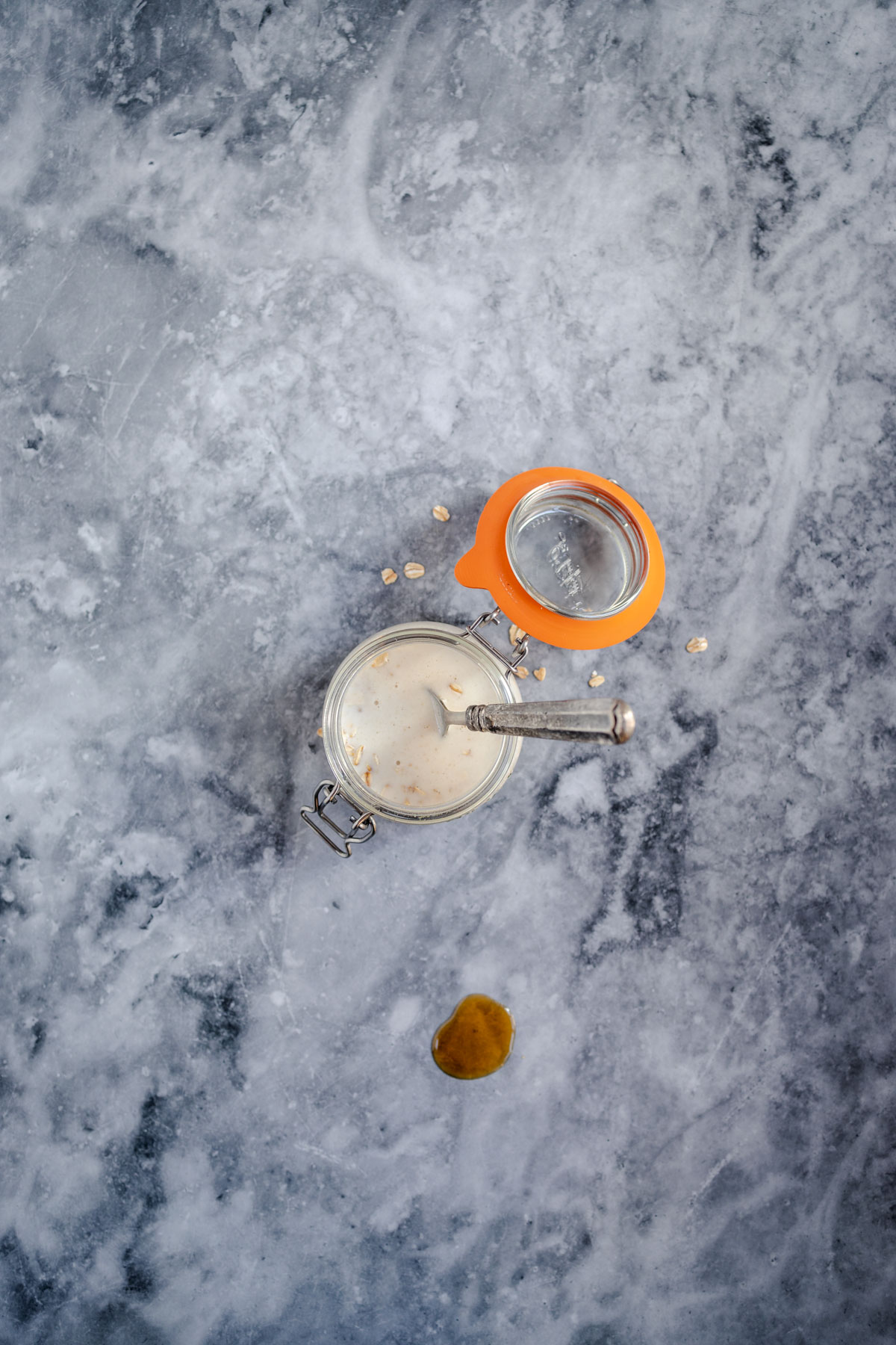 An overhead view of a spilled jar of milk with loose pearls scattered around on a marbled surface.