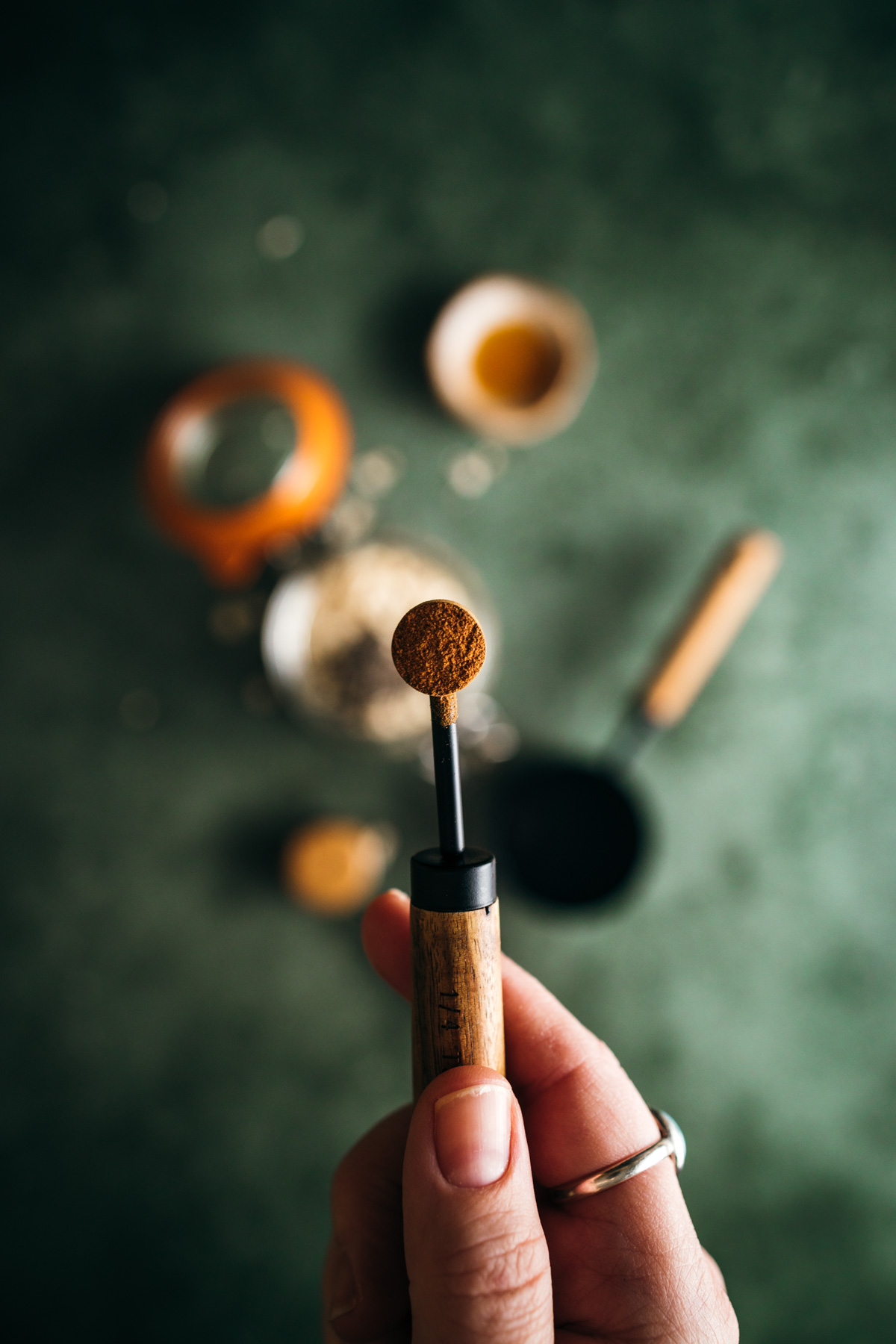 A person holding a measuring spoon with ground coffee over a coffee maker setup.