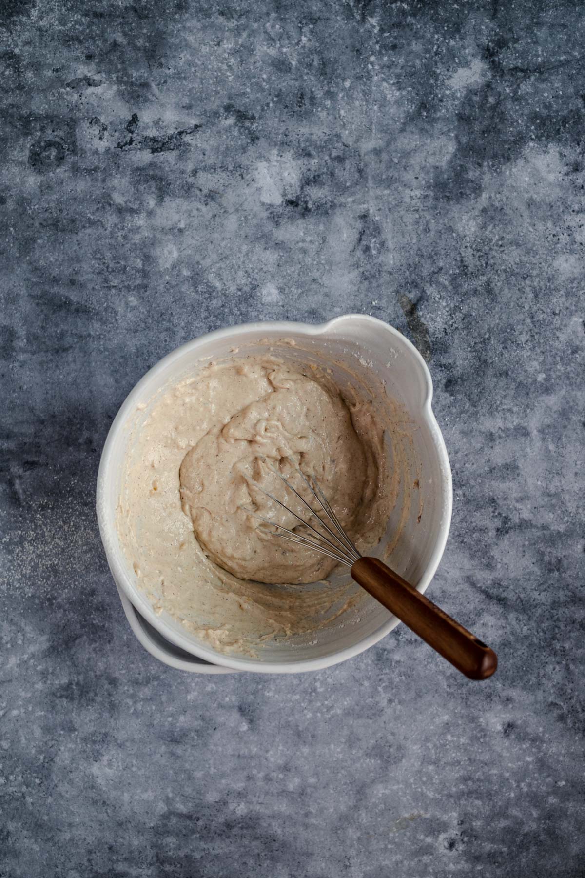 Bowl of batter with a whisk on a textured gray surface.