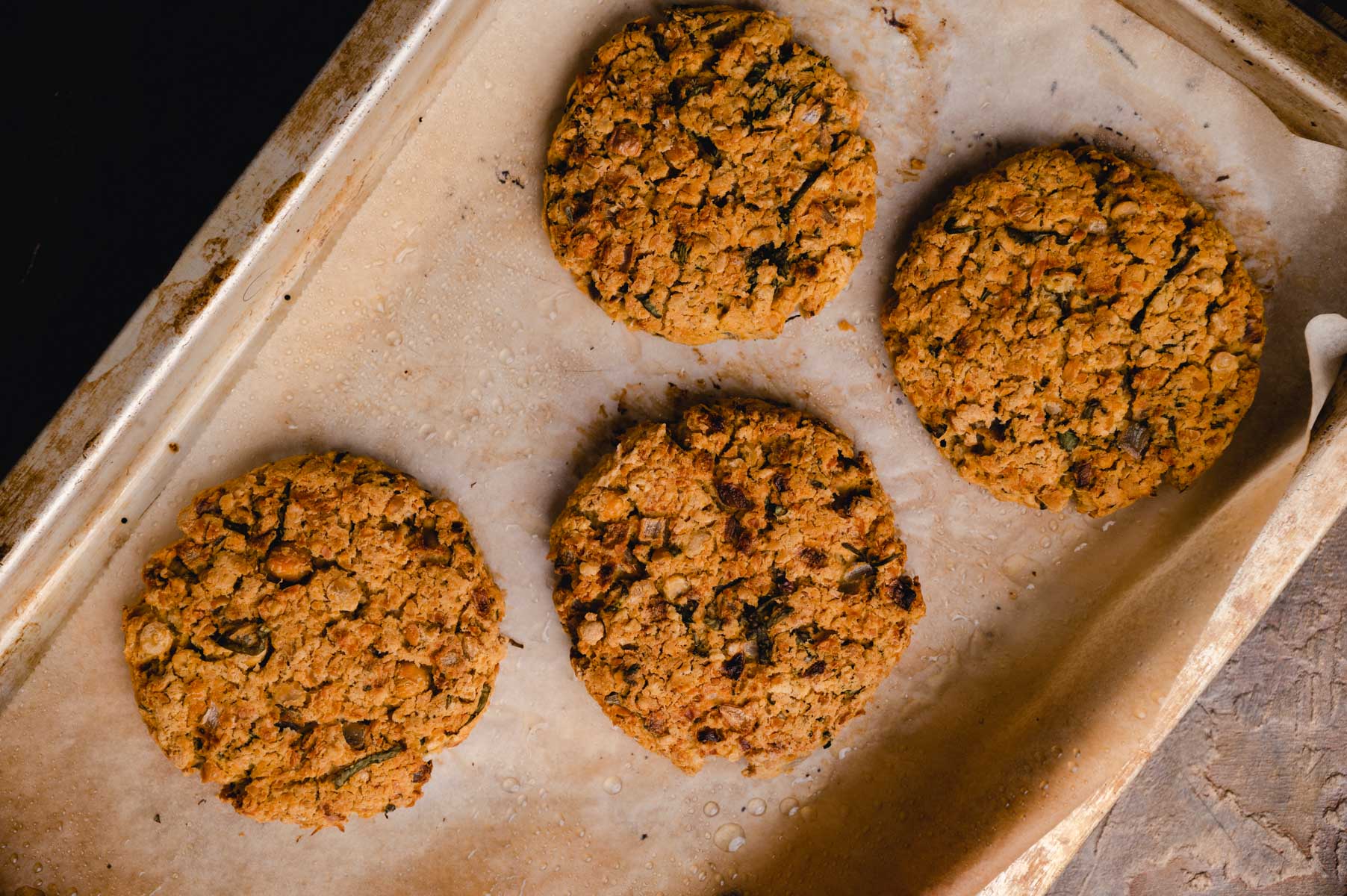 Four freshly baked oatmeal raisin cookies on parchment paper on a baking tray.