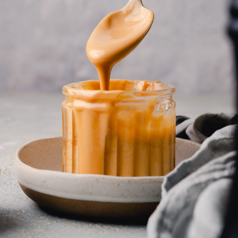 A spoonful of nut butter is being drizzled into a glass jar.