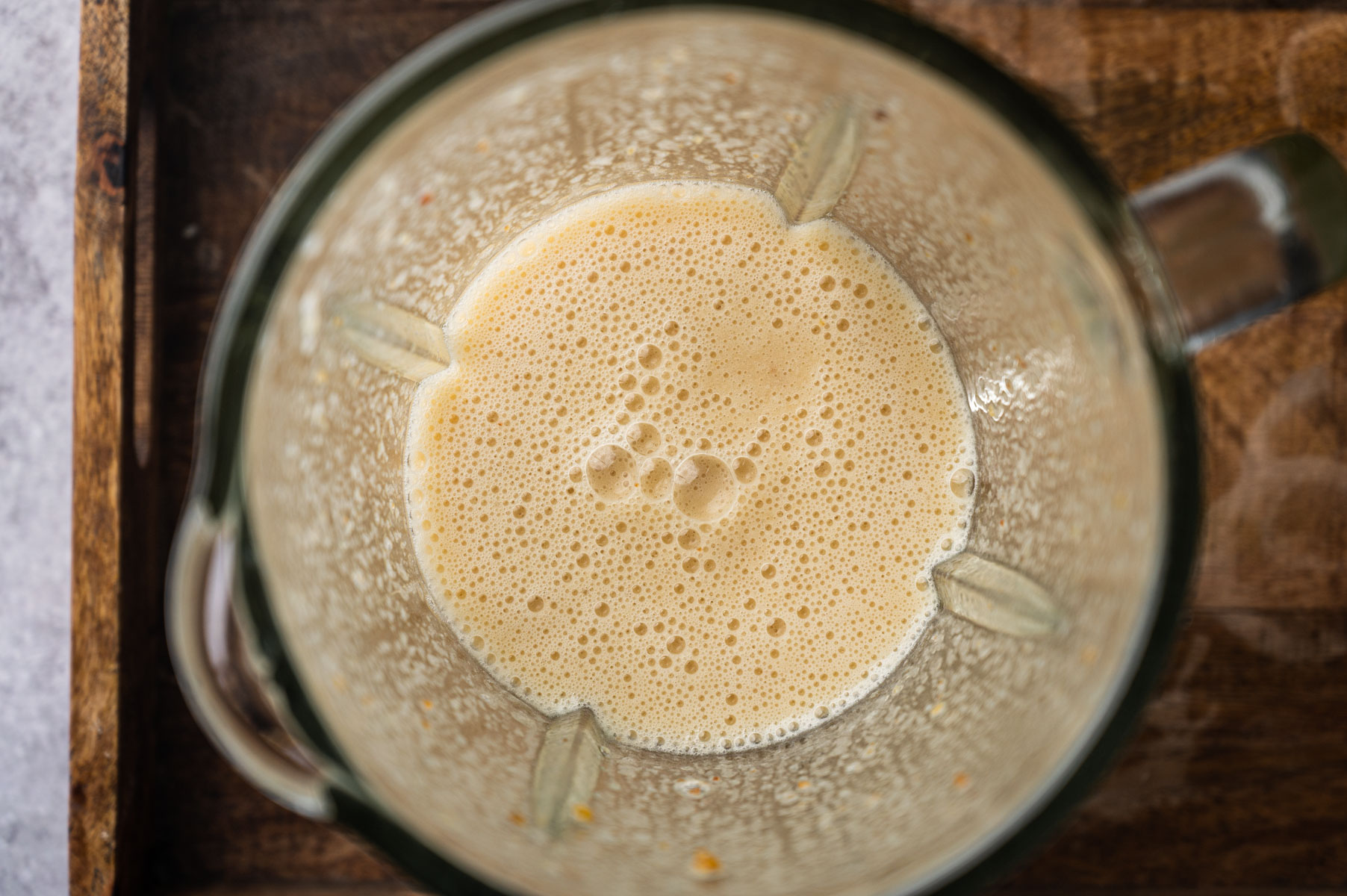 Top view of a blender with a frothy, light brown liquid inside, placed on a wooden surface.