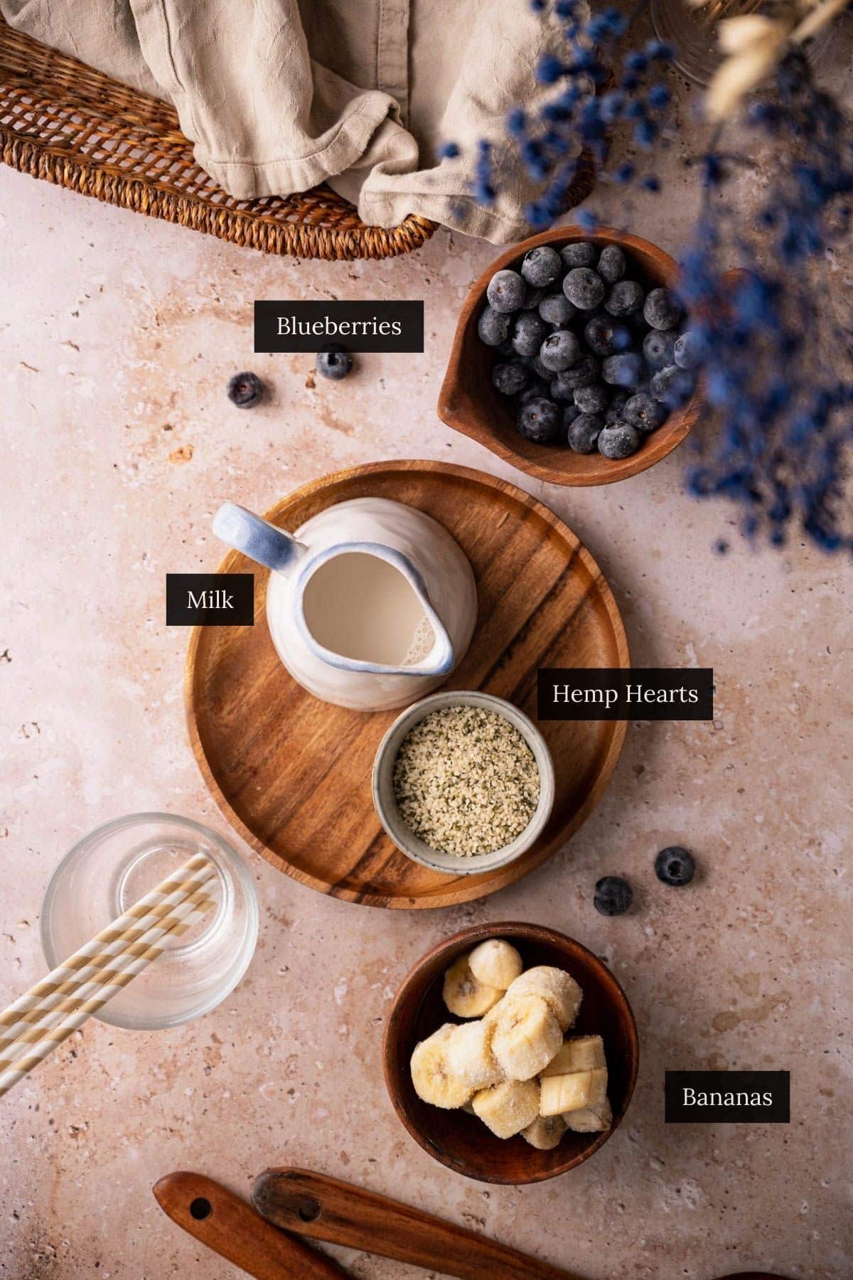 Top-down view of a table with a jug of milk, bowl of blueberries, hemp hearts, and banana pieces.