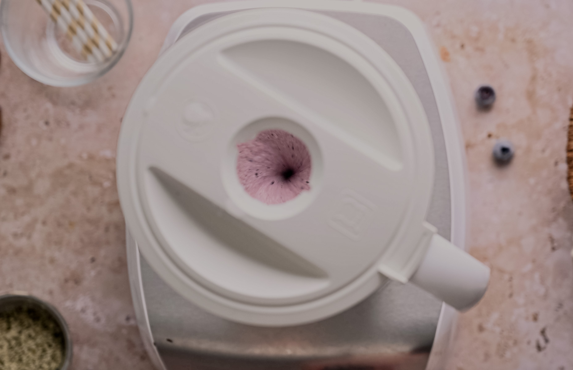 Top view of a blender with a smoothie and blueberries on the counter.