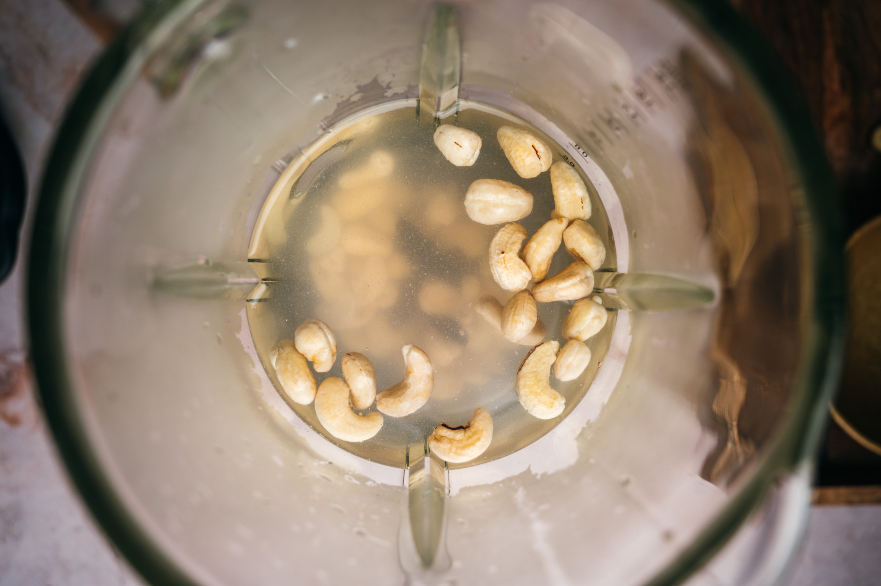 Top-down view of cashew nuts soaking in water inside a blender jug.