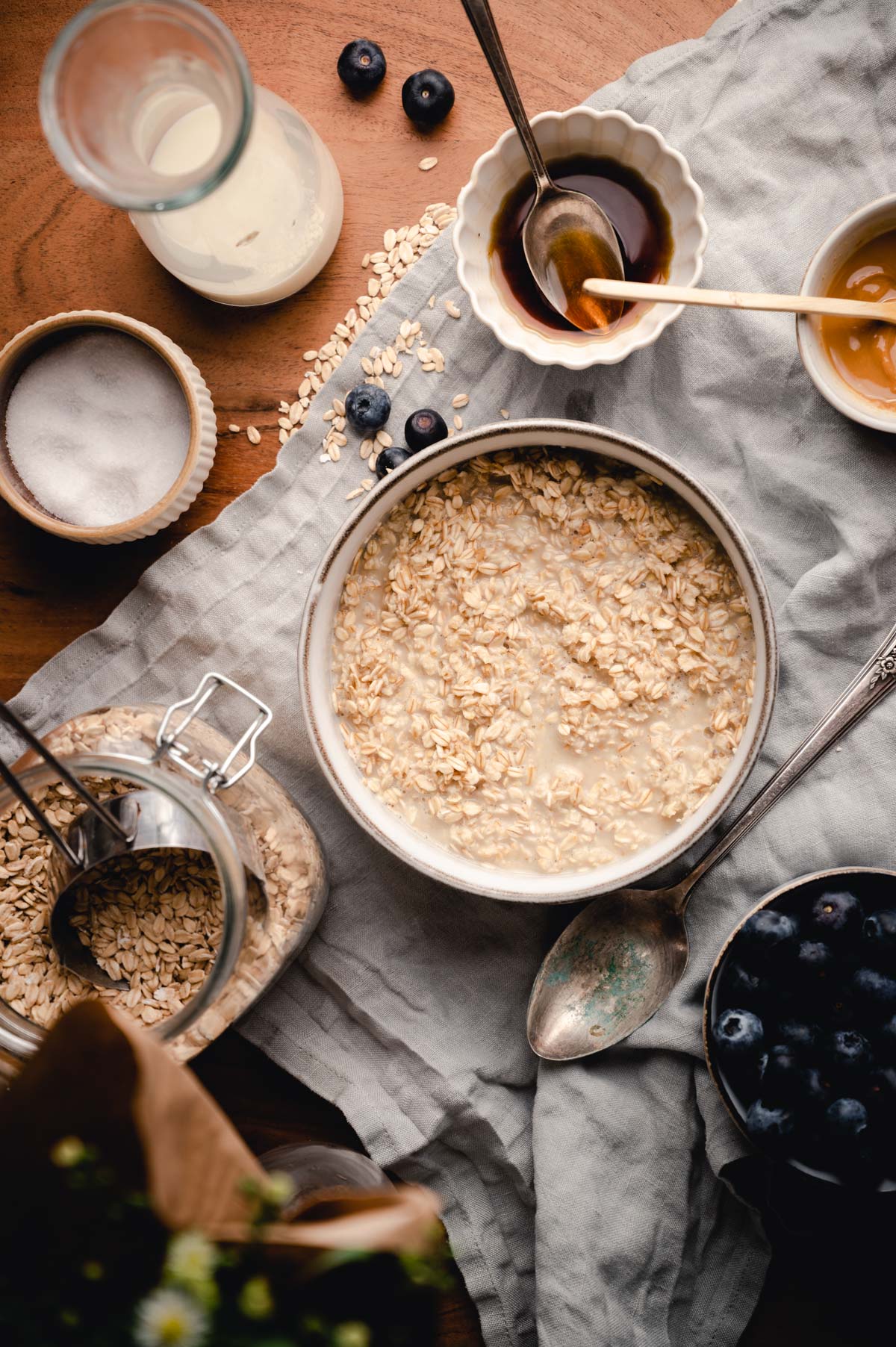 A cozy breakfast scene with a bowl of oatmeal, honey, milk, and fresh blueberries on a wooden table.