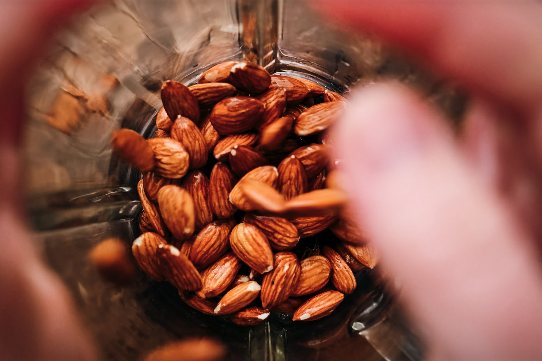 Whole almonds in a transparent blender jar, viewed from the top with a slight blur in the foreground.
