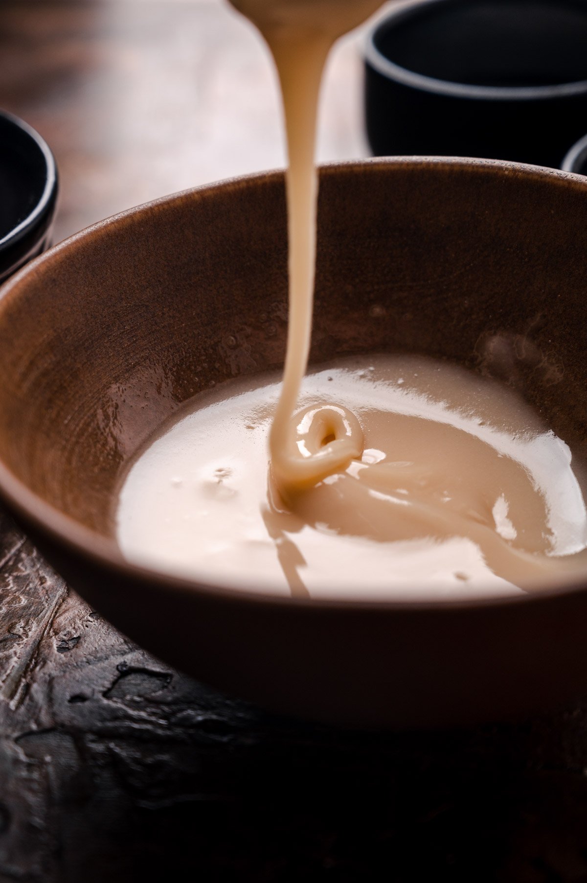 Maple glaze drizzling off of a spoon into a bowl.