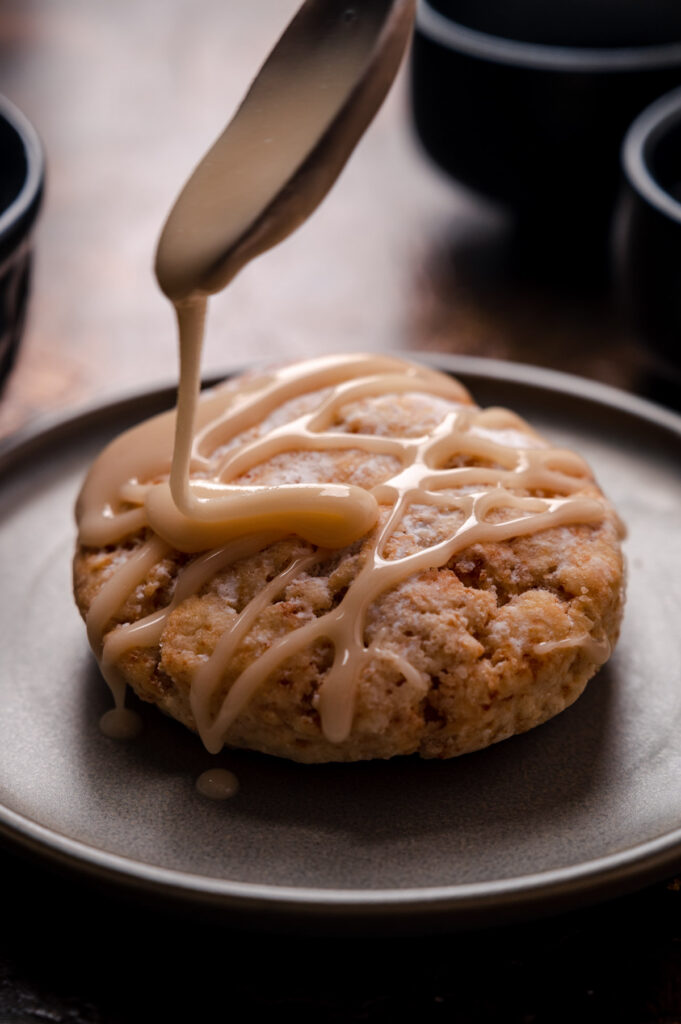 Spoon drizzling maple glaze onto a scone.