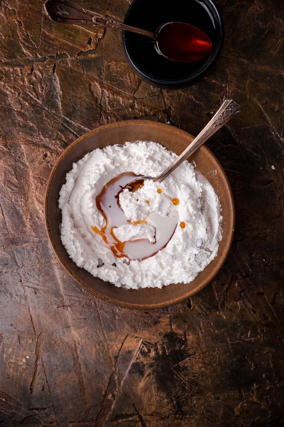 Rice pudding in a rustic bowl, topped with caramel sauce and orange zest, served with a spoon on a textured dark surface.