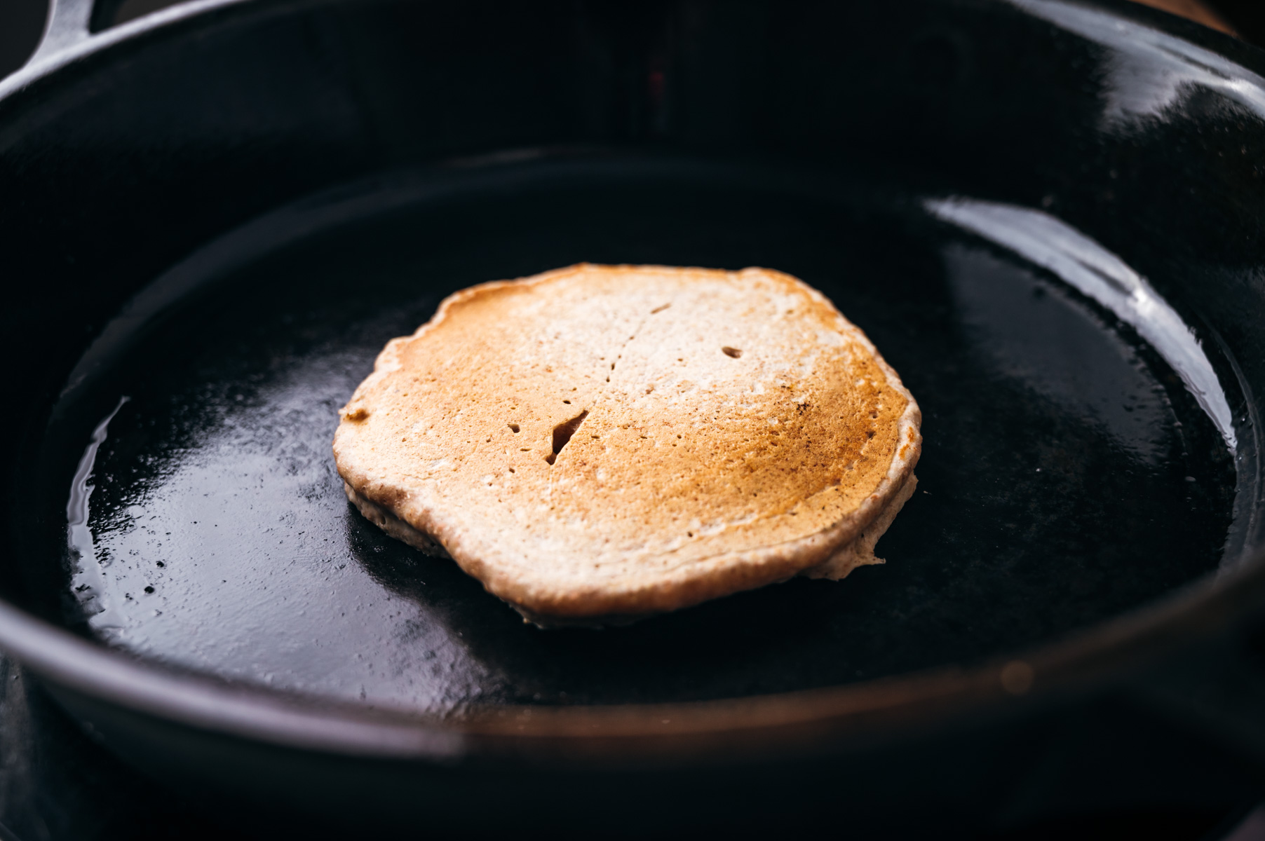 A pancake cooking in a black skillet.
