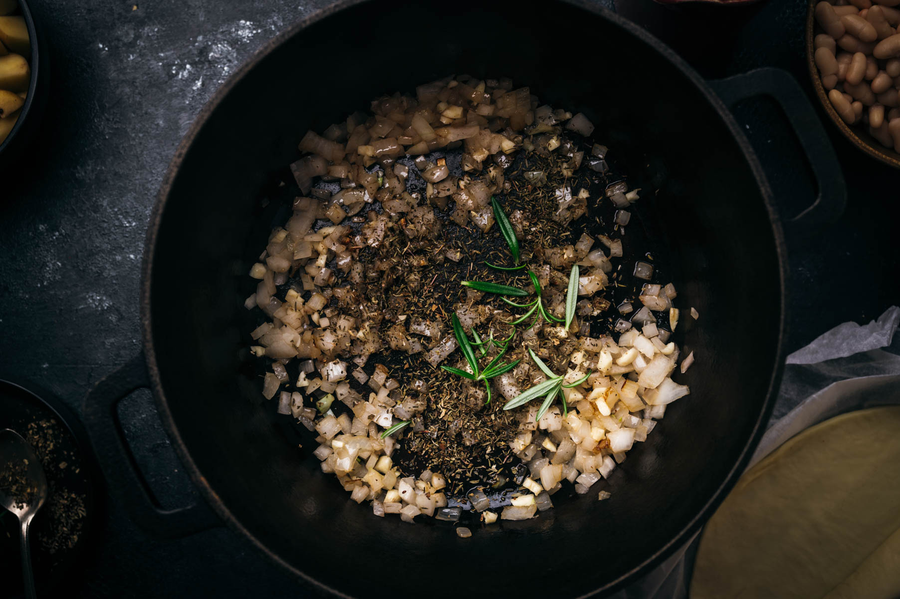 Diced onions and herbs cooking in a black cast iron pot, viewed from above.