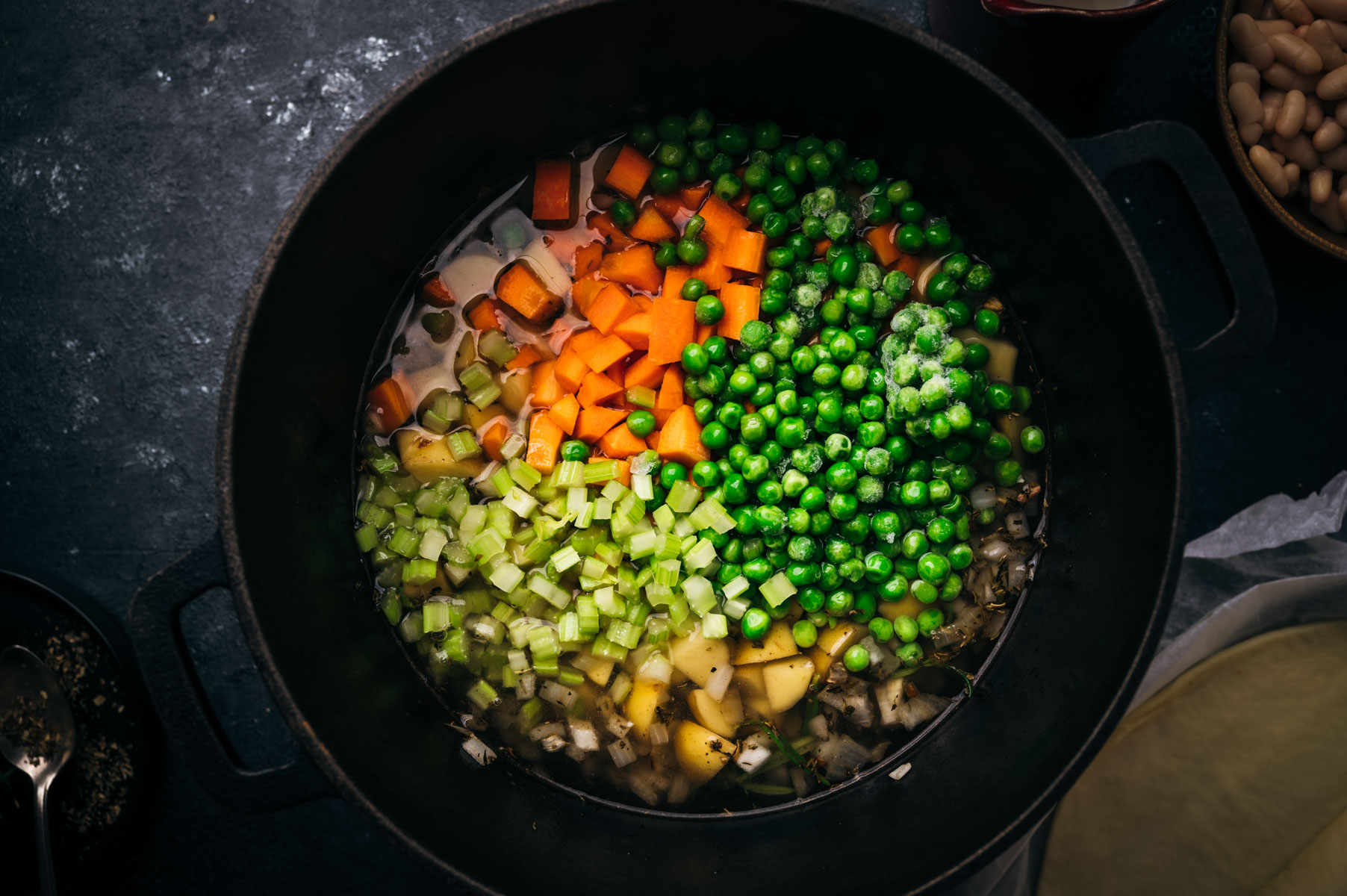 A pot filled with diced vegetables including carrots, peas, celery, and potatoes, with a focus on vibrant colors and textures.