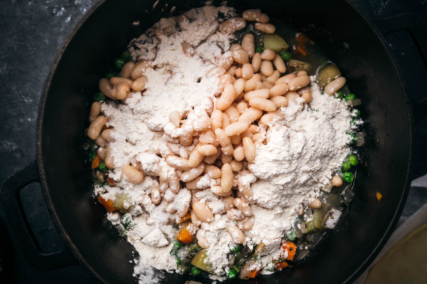 A pot with a mixture of white beans, diced vegetables, and flour, viewed from above.