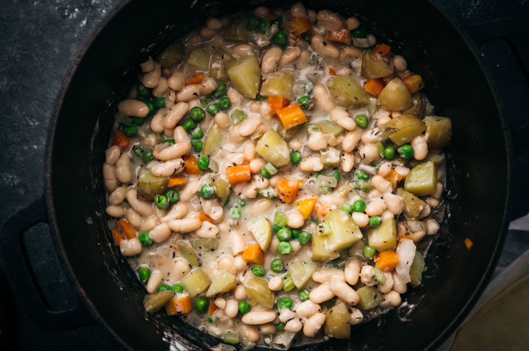 Top view of a pot containing a vegetable and bean stew, featuring carrots, peas, and potatoes.
