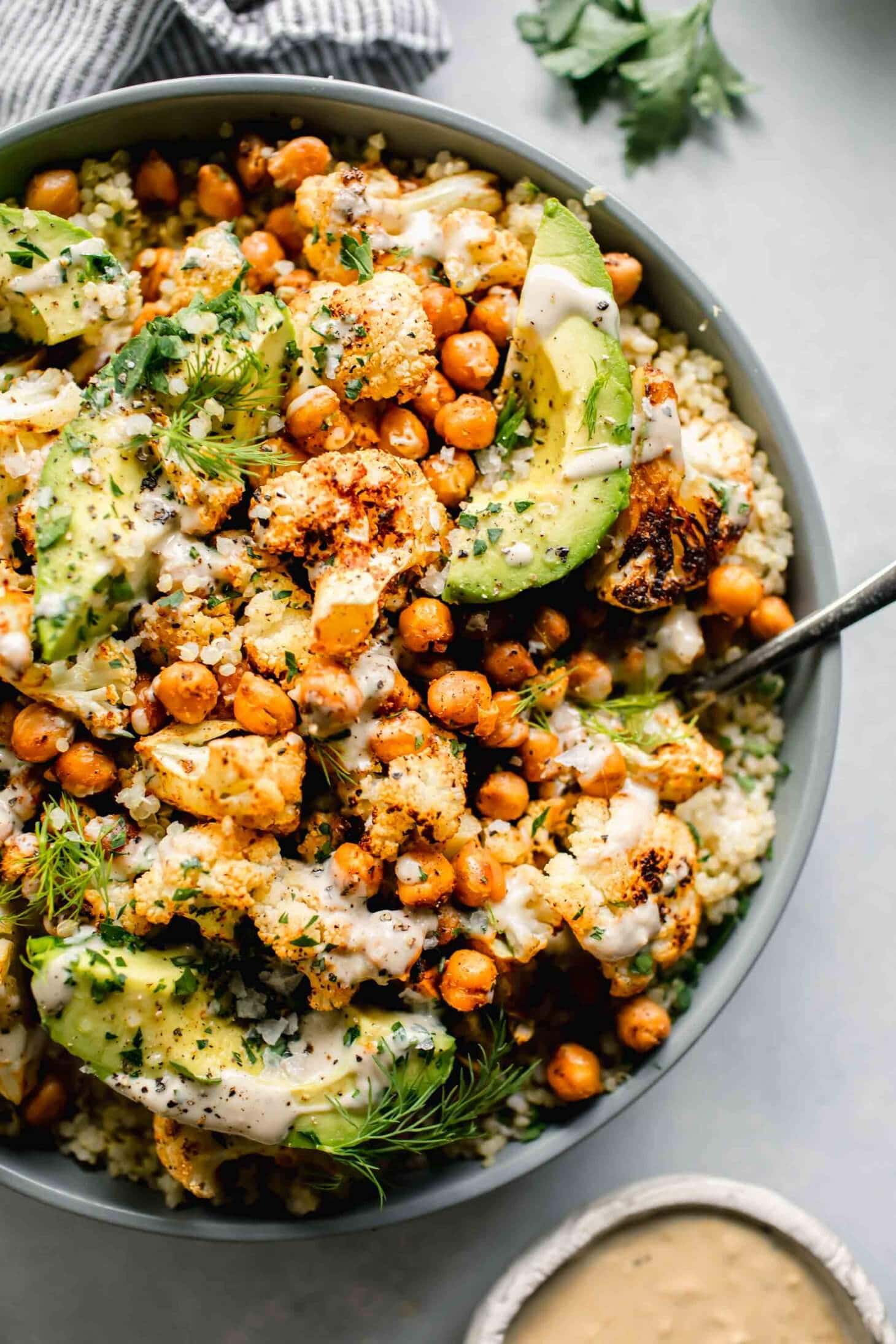 A bowl of quinoa topped with roasted cauliflower, chickpeas, avocado slices, fresh herbs, and a creamy dressing makes for one of those delicious dishes that you can also serve alongside a vibrant pasta salad.