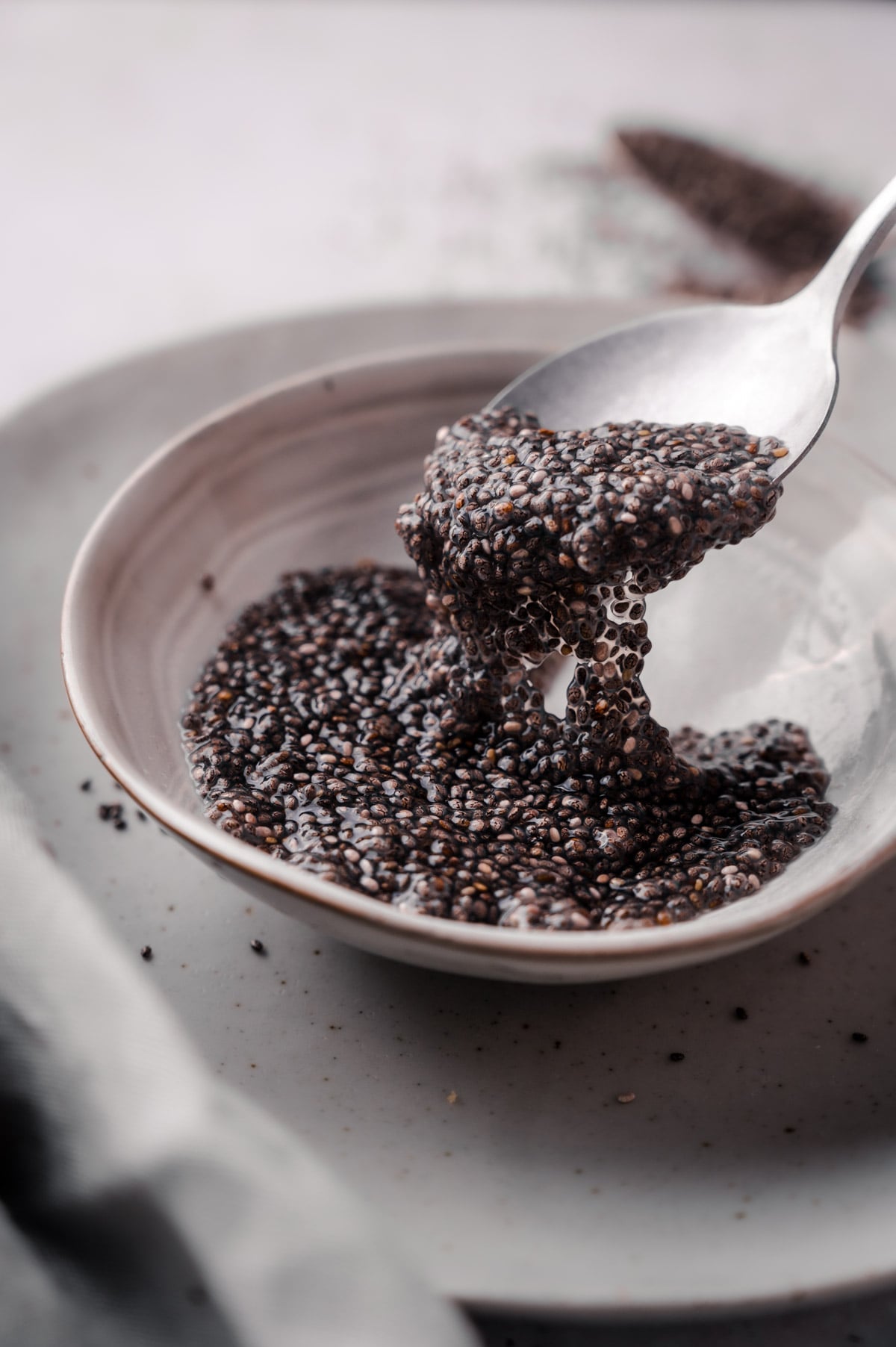 A spoon scooping hydrated chia seeds from a white bowl on a light-colored table.