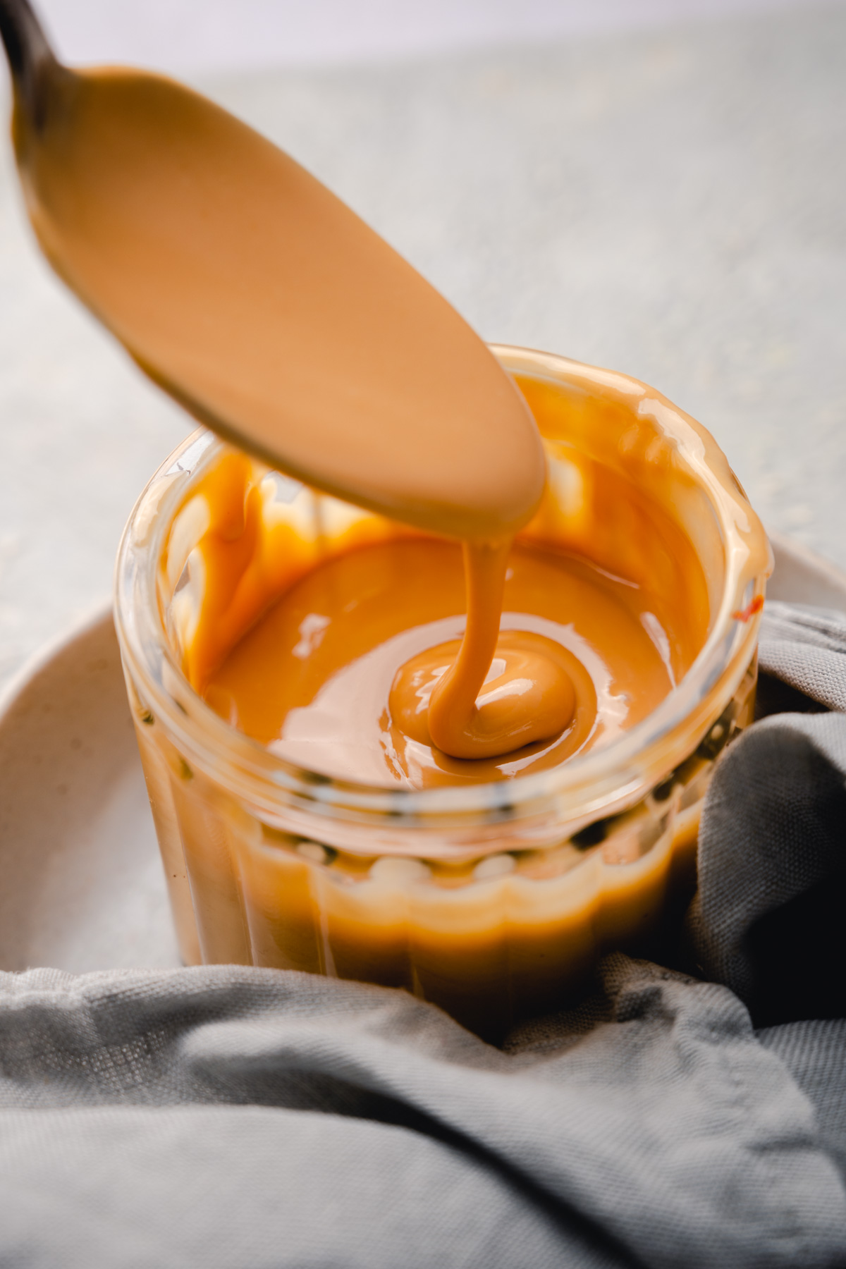 A spoon dipped in a jar of almond butter, with it dripping back into the jar.