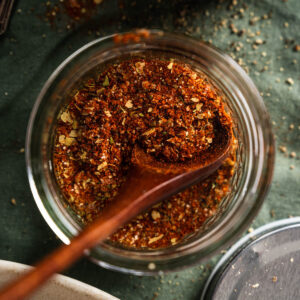 A wooden spoon inside a glass jar filled with a mix of ground spices.