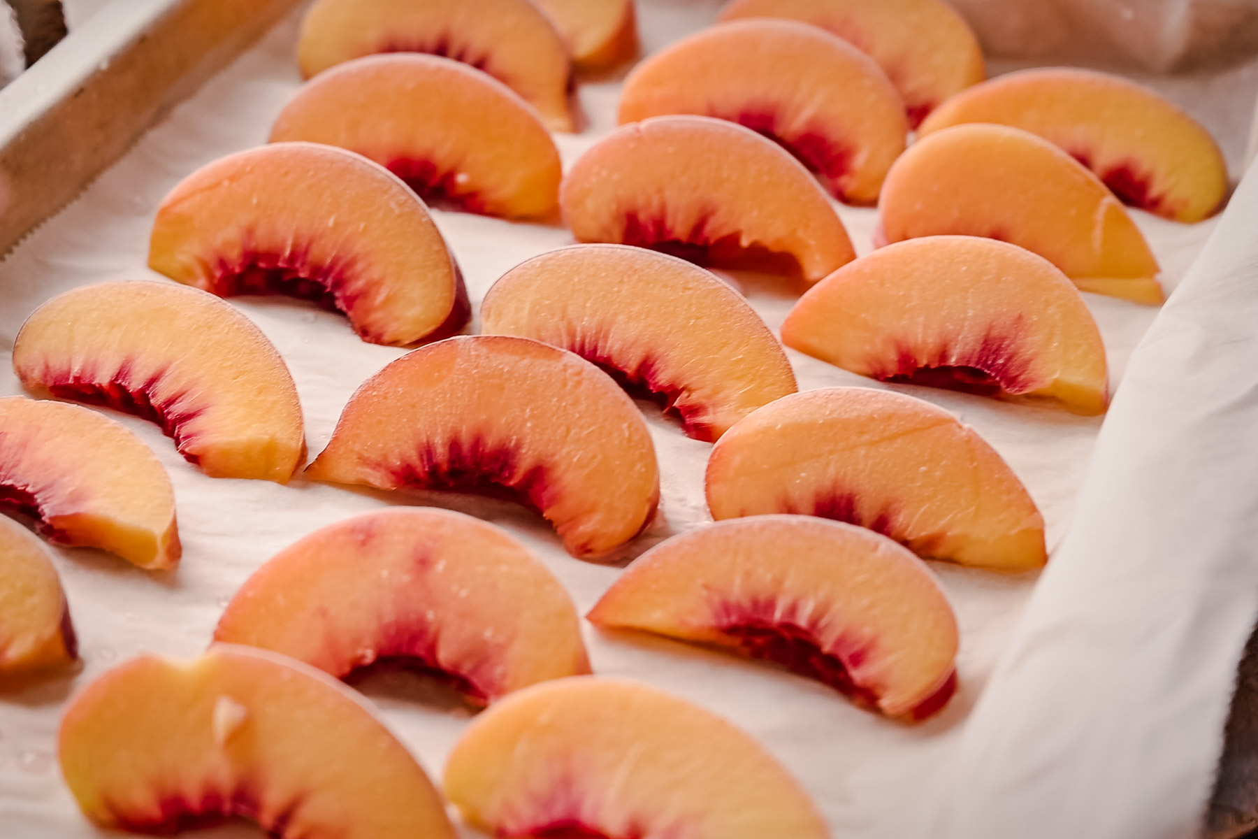 Sliced peaches arranged on a parchment paper-lined baking sheet.