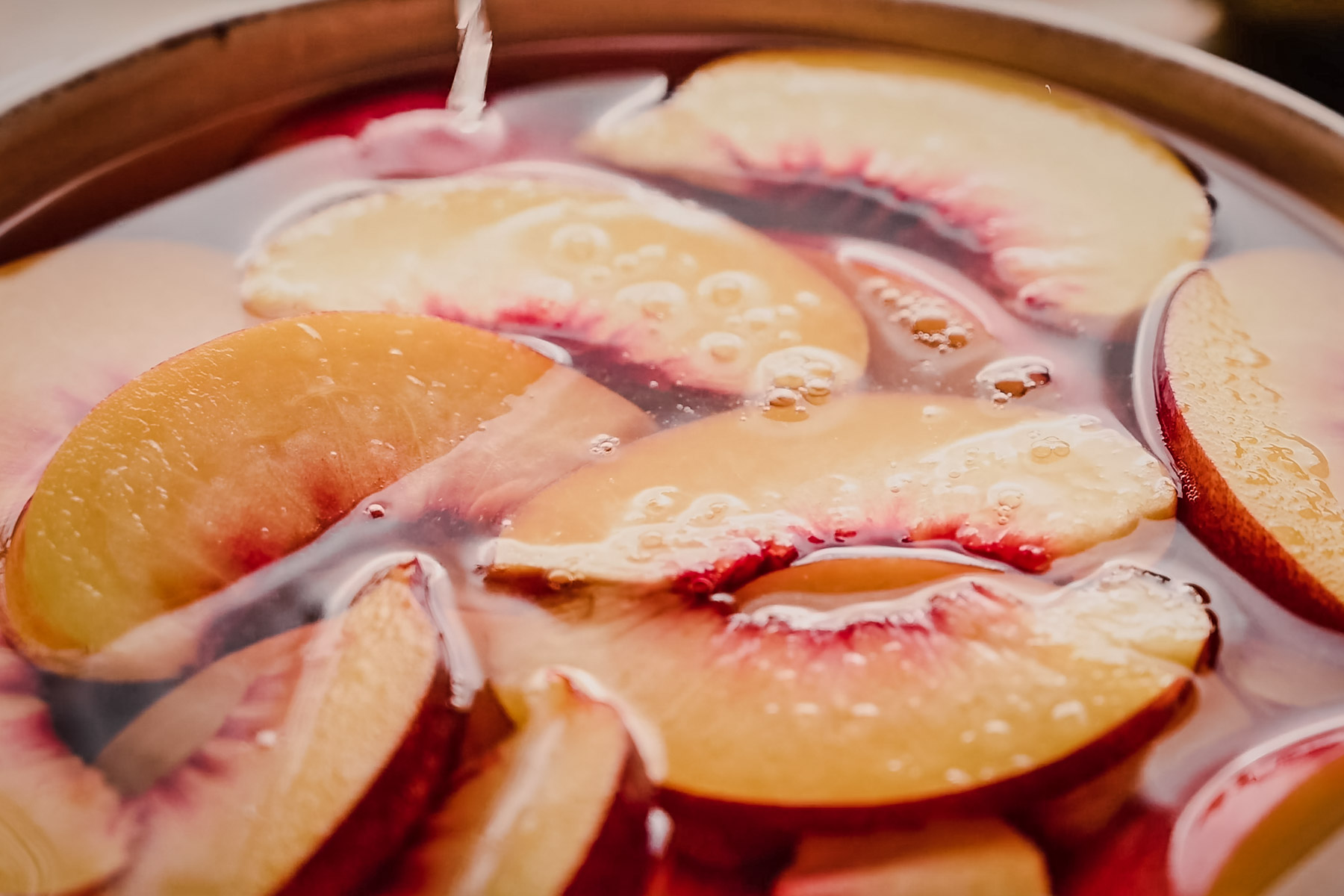 Close-up of sliced peaches soaking in liquid. The peach slices are partially submerged and surrounded by bubbles.