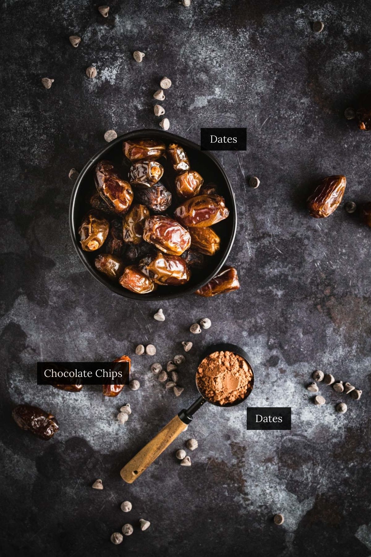 A bowl of dates next to a measuring cup filled with chocolate chips and cocoa powder on a dark textured surface.