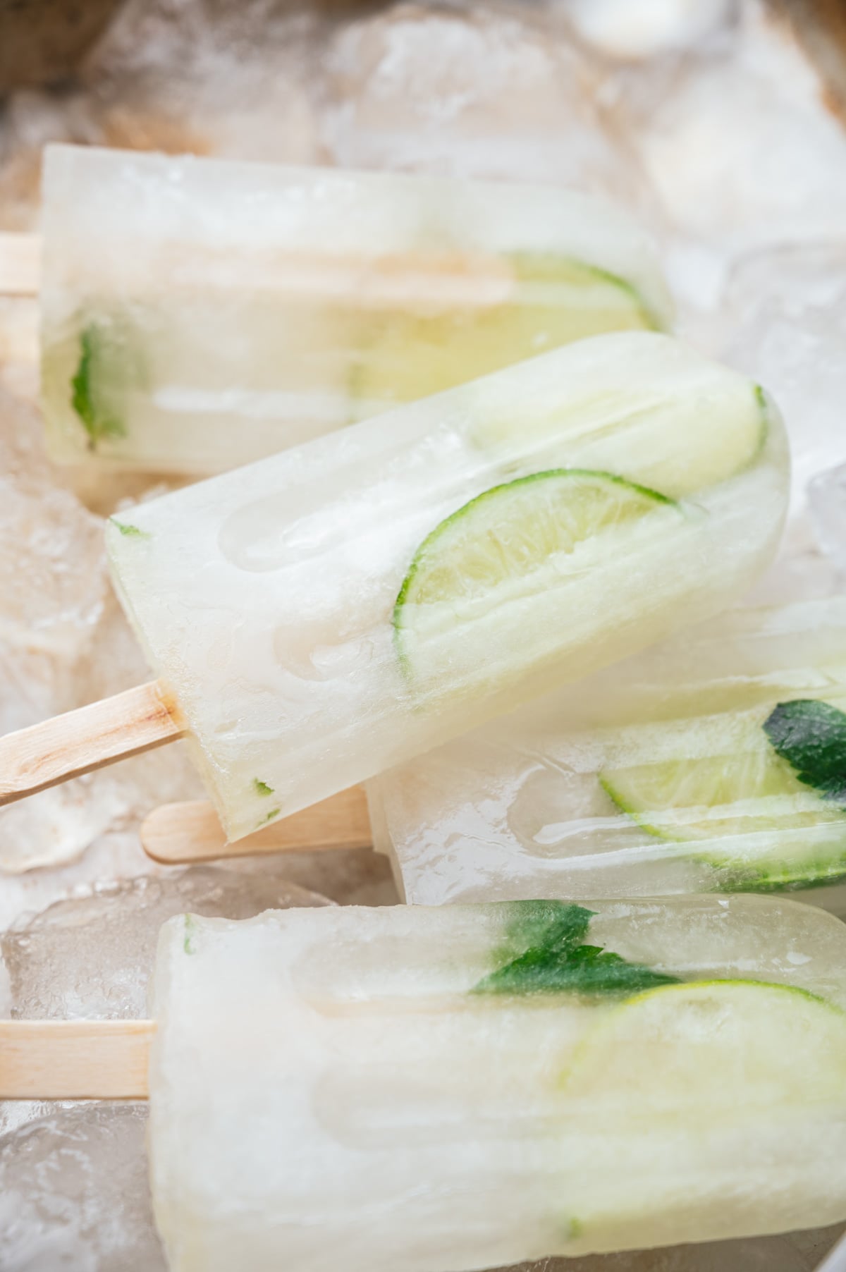 Close-up of ice pops with visible slices of lime and mint leaves inside, placed on a bed of ice.
