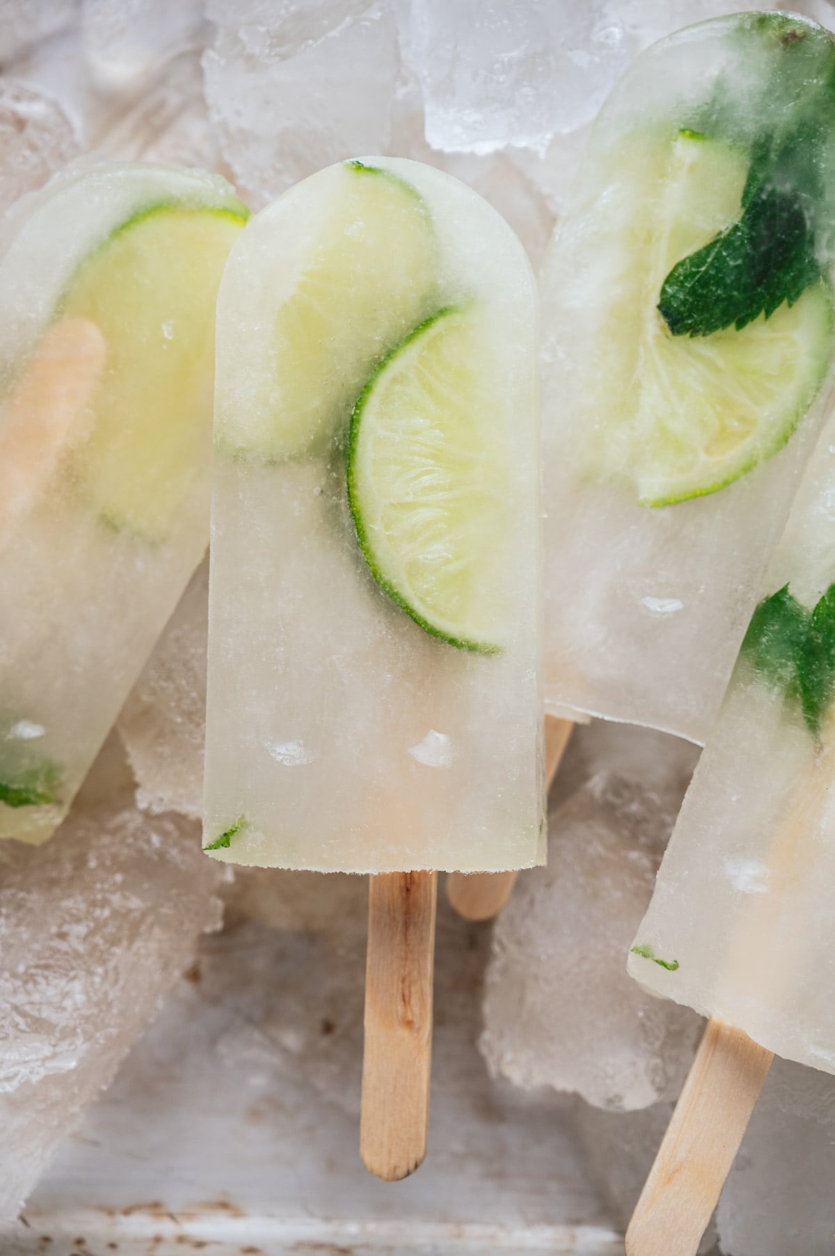 Close-up of lime popsicles with lime slices and mint leaves inside, resting on ice cubes.