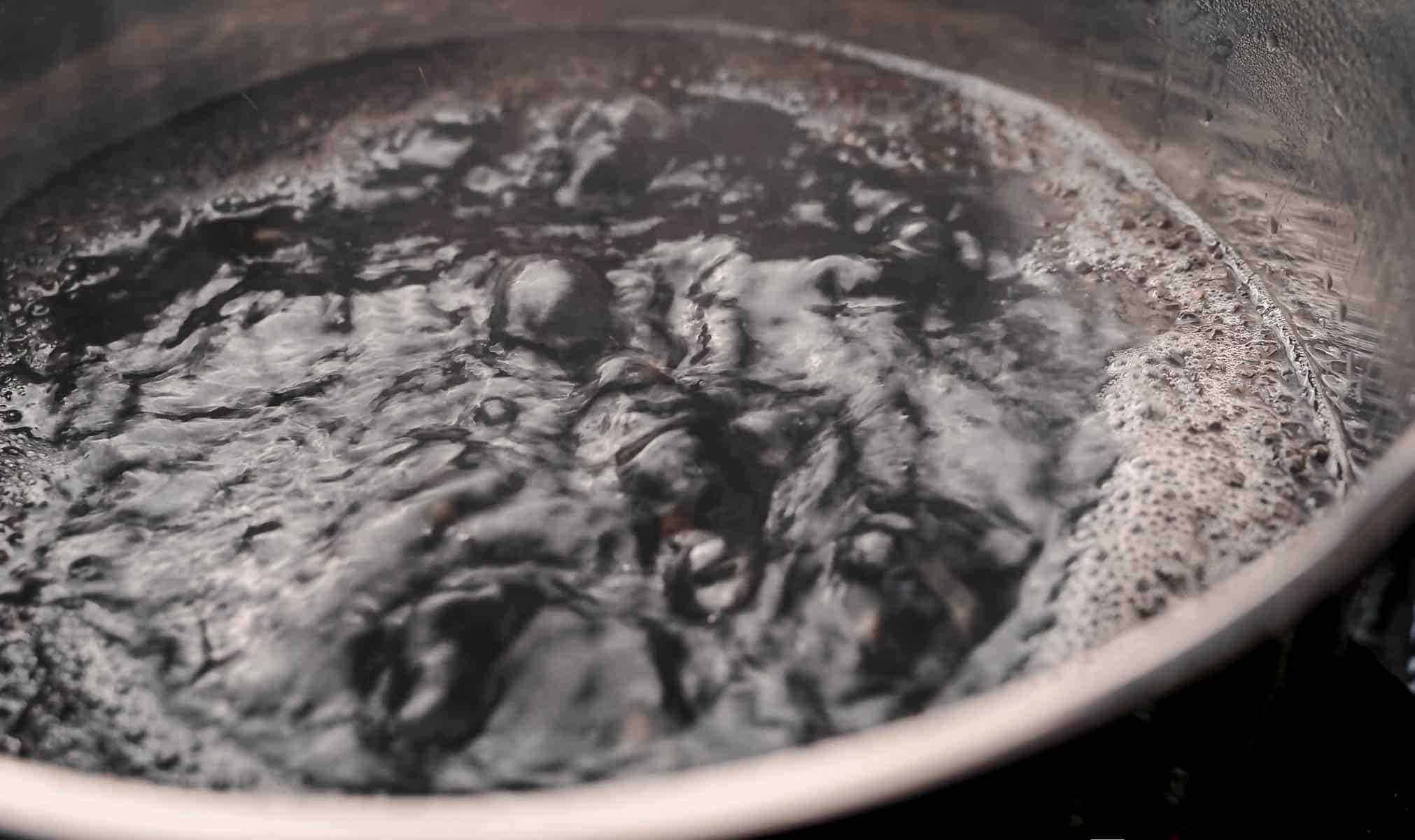 Close-up view of a pot of boiling water and lentils with steam rising on the surface.