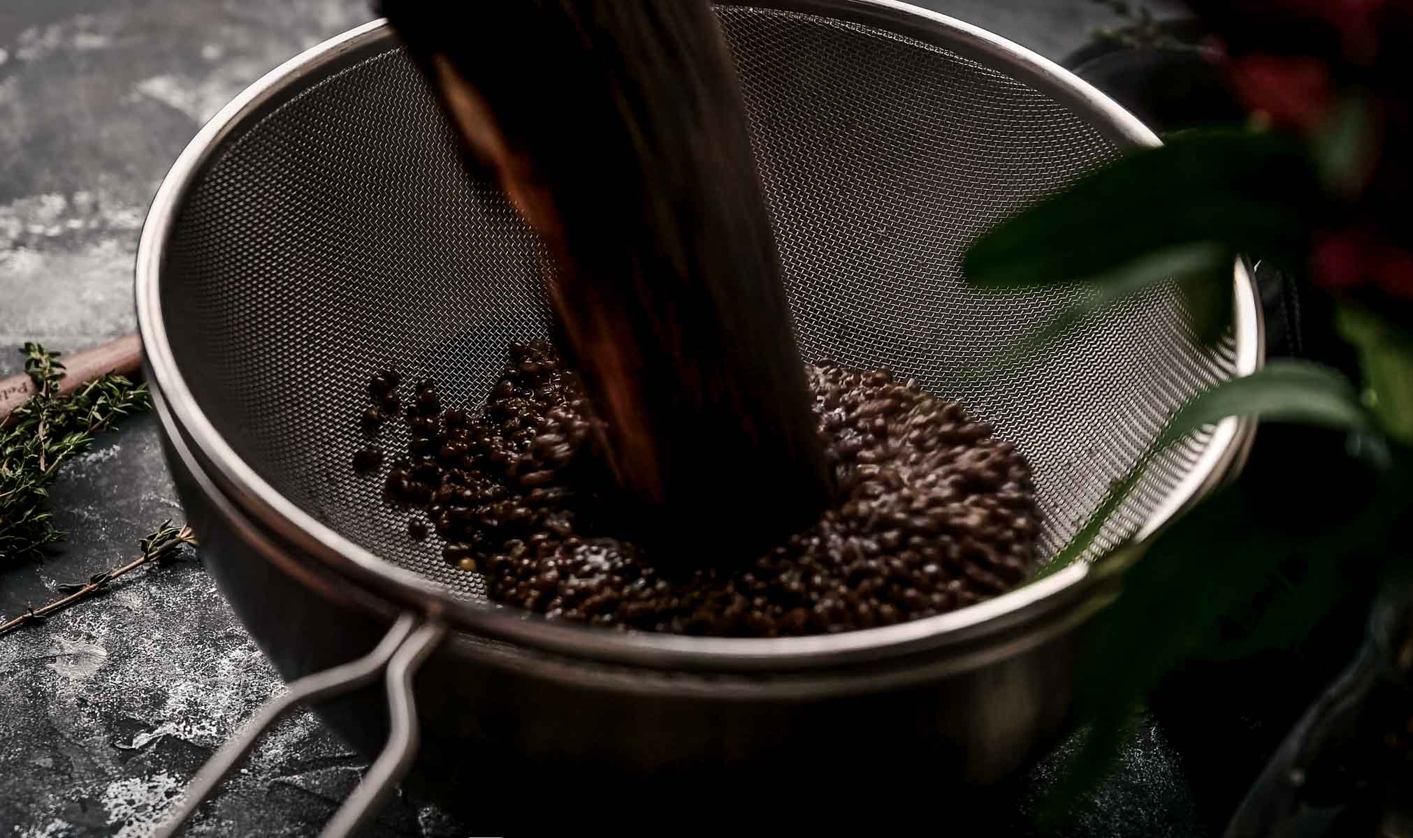 Cooked lentils being poured into a fine mesh strainer over a dark surface.