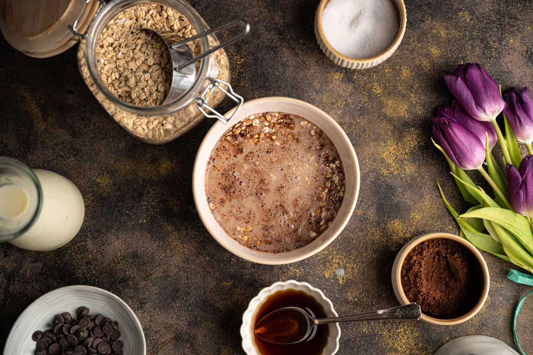 A bowl of oats mixed with milk sits on a dark surface.