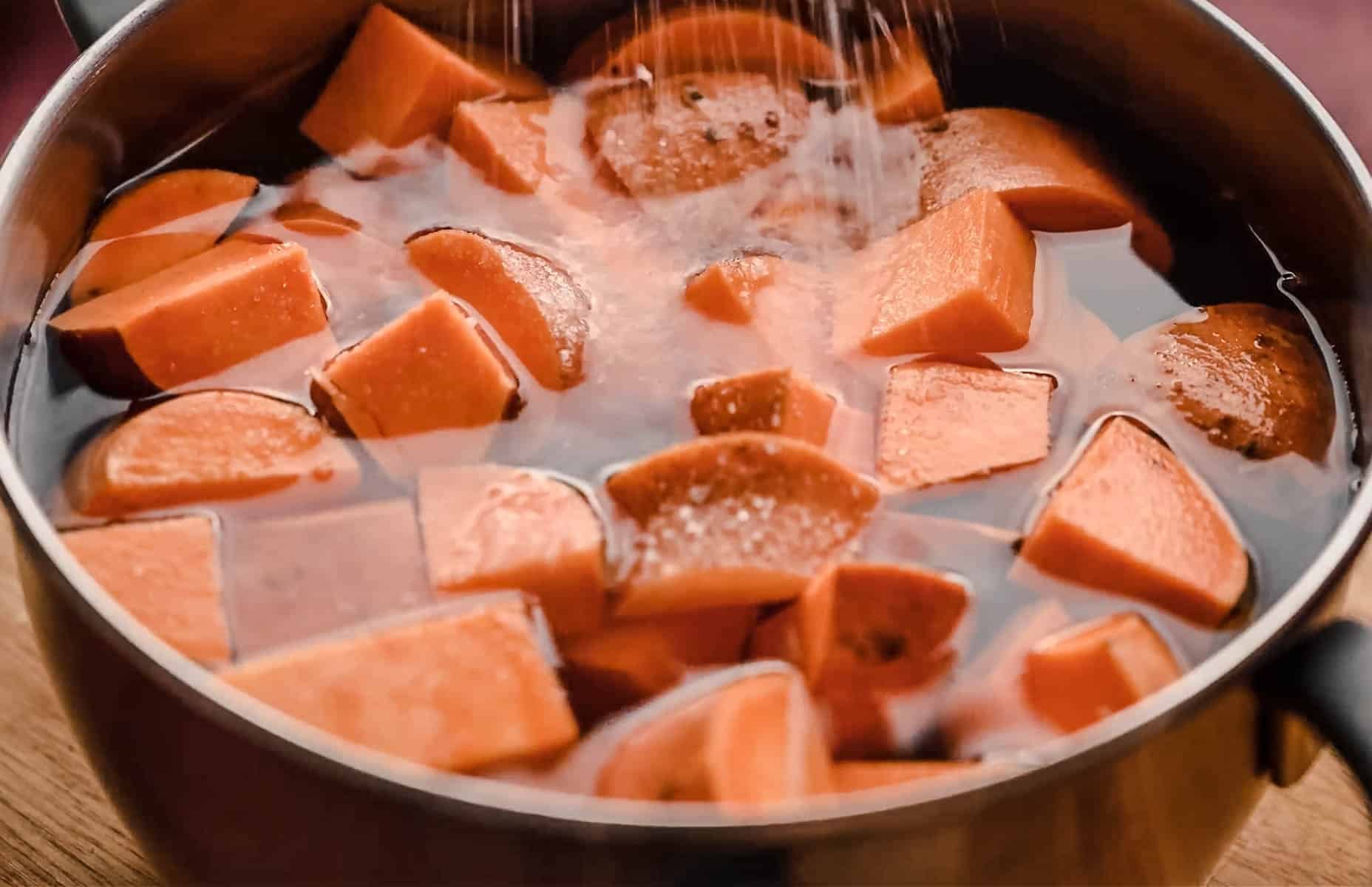 A pot filled with water and cubed sweet potatoes is shown, with salt being sprinkled on top.